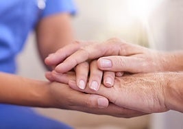 Una enfermera y una paciente juntan sus manos.