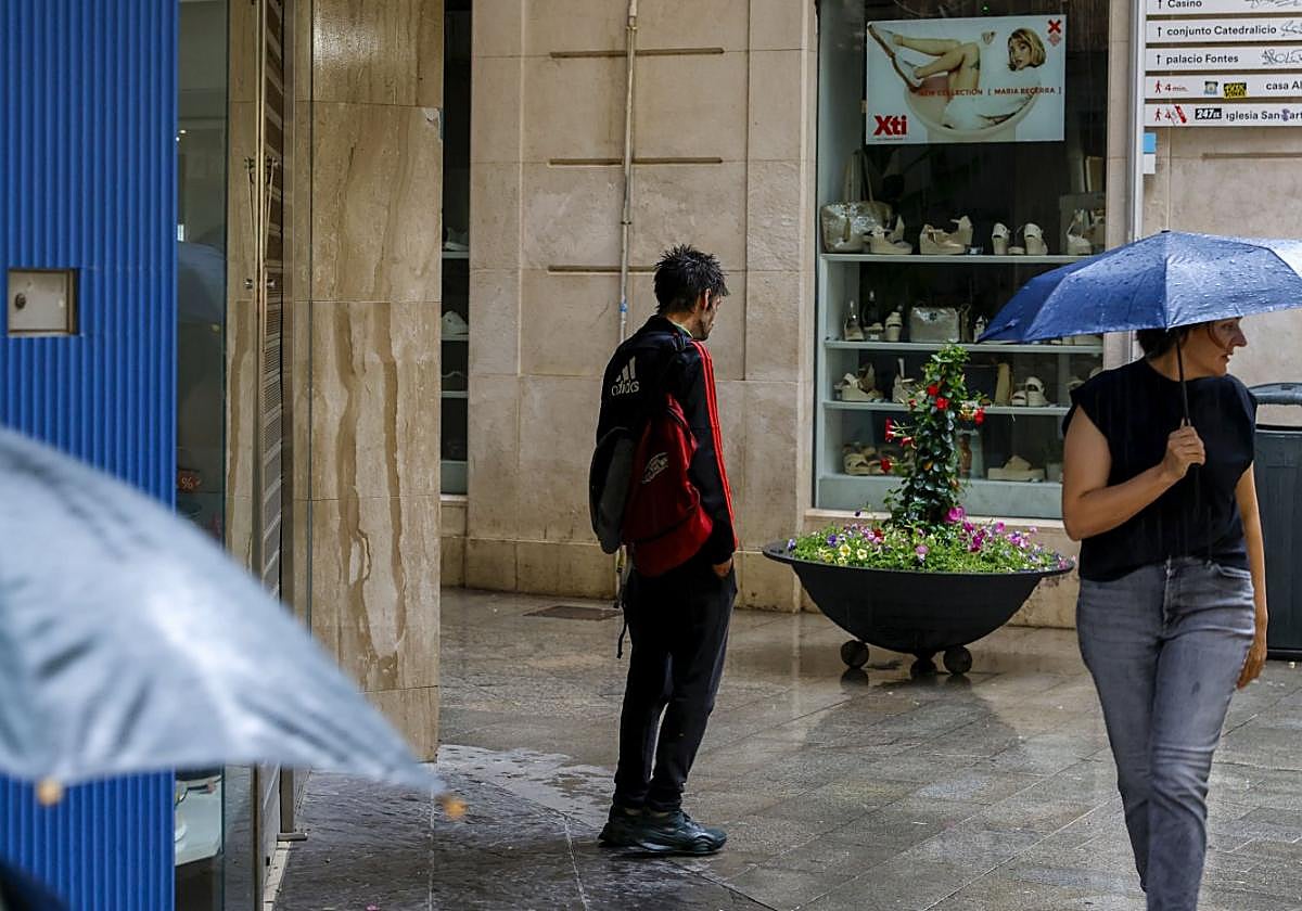 Una persona sin hogar (centro de la imagen) se resguarda de la lluvia, el pasado viernes, bajo una cornisa en el centro de Murcia.