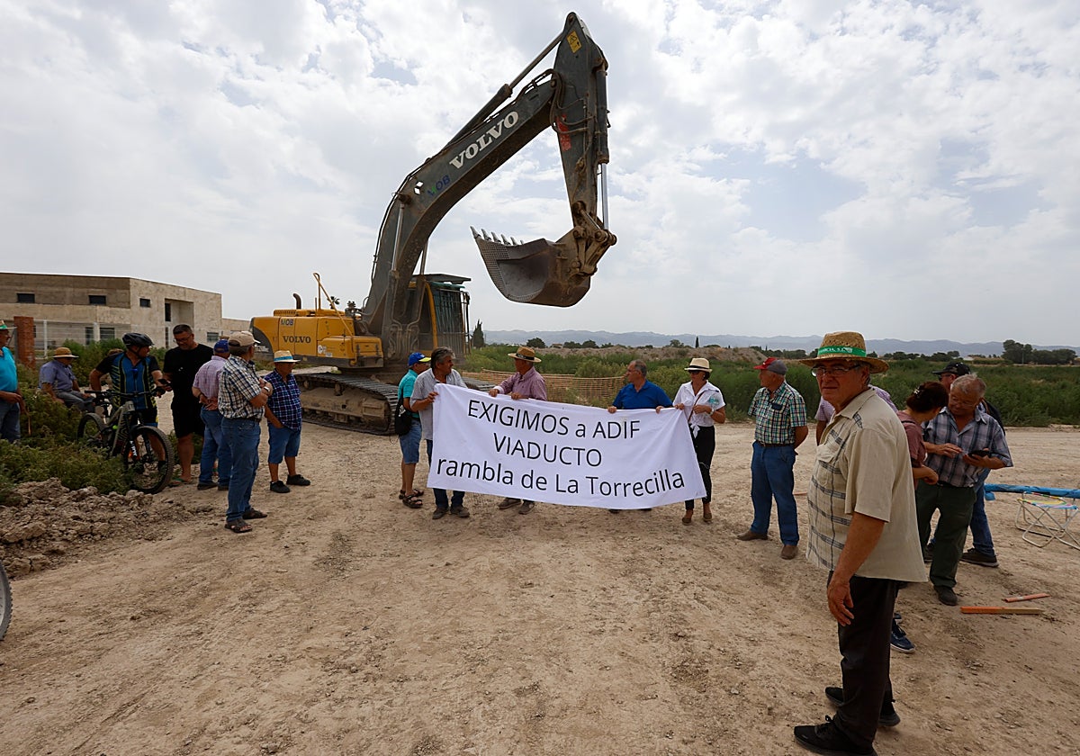 Una pala retroexcavadora pasa junto a los vecinos concentrados en la rambla de La Torrecilla donde se construye la plataforma del AVE.