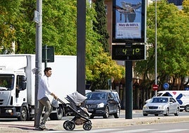 Un hombre cruza un paso de peatones empujando un carrito de bebé, junto a un termómetro que marca 41 grados en Murcia.