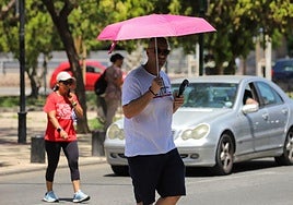 Peatones cruzan una calle en Murcia resguardándose del sol.
