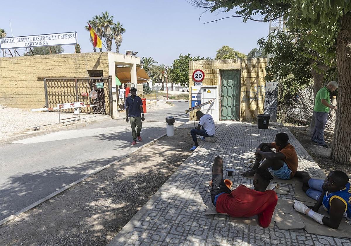 Un grupo de migrantes aguarda a la sombra frente al acceso principal al Hospital Naval.
