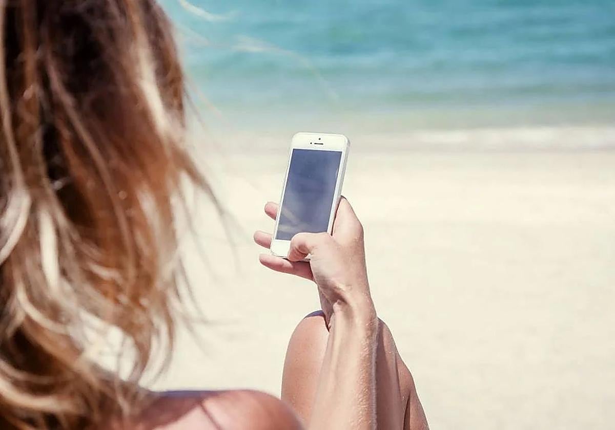 Una mujer consulta su móvil en la playa.