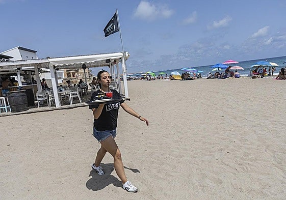 Una camarera camina por la arena de la playa de Levante los 50 metros que separan el quiosco de las hamacas, tal y como exige este año Costas.