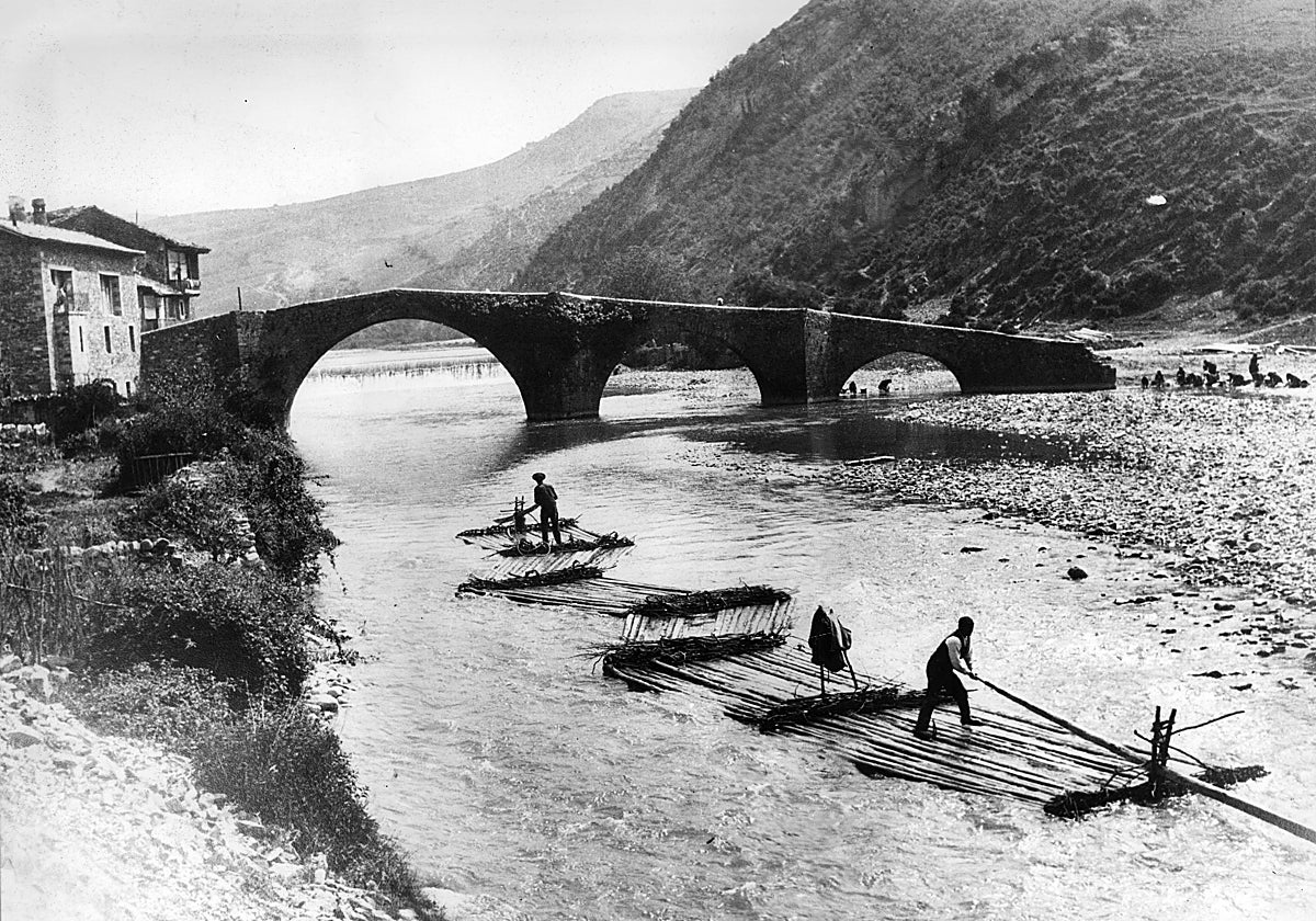 De los valles pirenaicos navarros de Roncal, Salazar y Aézcoa se bajaba la madera por los ríos para su aprovechamiento. En la imagen, almadia y balsas a su paso por el puente romano del río Esca (arriba, a la derecha, un grupo de lavanderas) en la villa navarra de Burgui, pórtico de entrada al Valle de Roncal.