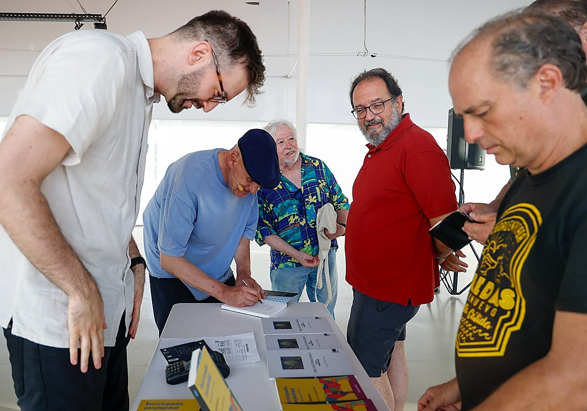 Imagen principal - Antón Reixa firma ejemplares de su antología, traducida por Xabier Cordal, y con Lara López en su encuentro en Cartagena.