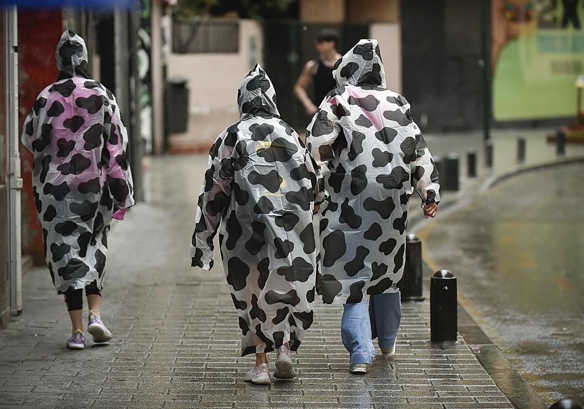 Tres peatones caminan por el centro de Murcia cubiertos con chubasqueros.