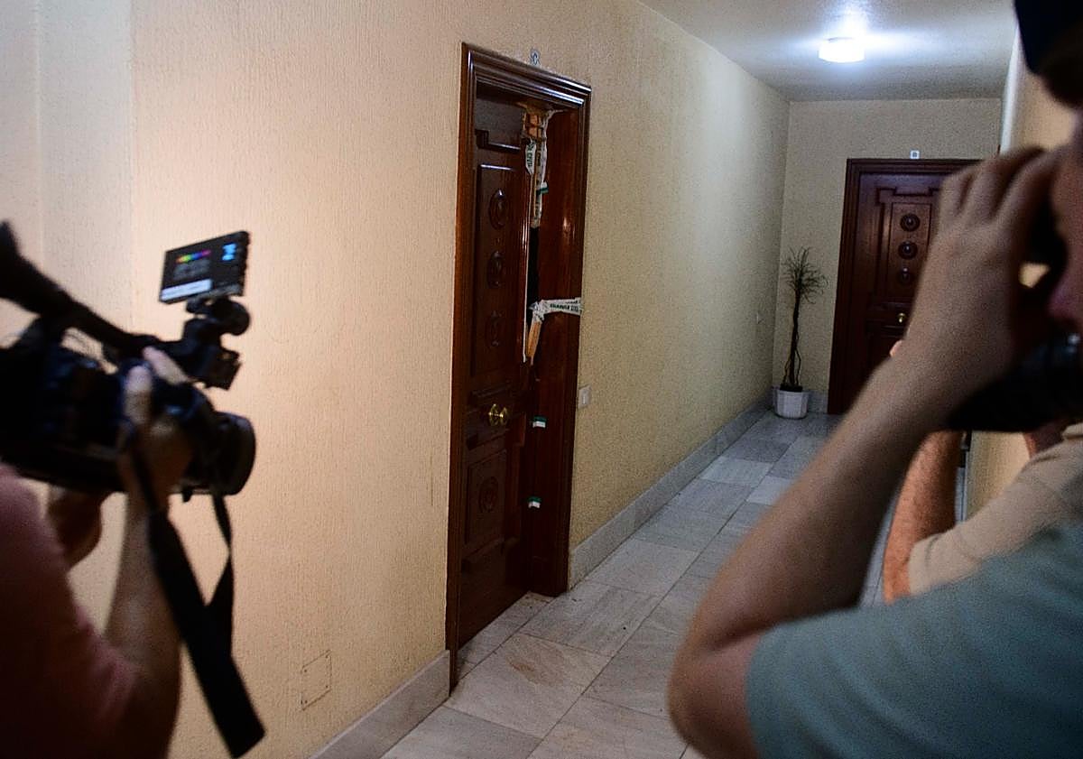 Imagen principal - Arriba, la puerta de la casa donde se encontró el cadáver. Abajo, agentes en la entrada del edificio.