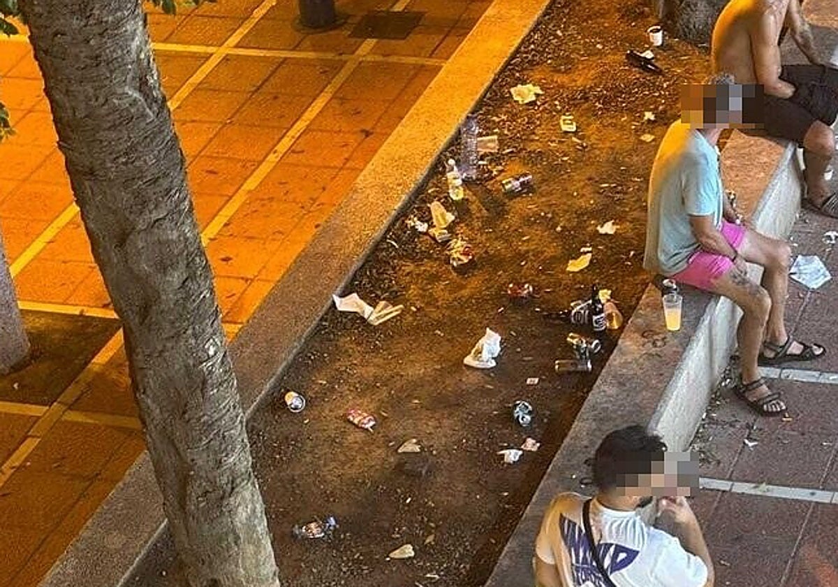 Varias personas en el exterior del local de apuestas con botellas, latas de bebida y vasos a su alrededor.