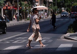Una mujer cruza un paso de peatones mientras se protege del sol con una sombrilla.