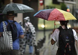 Peatones se protegen de la lluvia mientras caminan por Murcia.