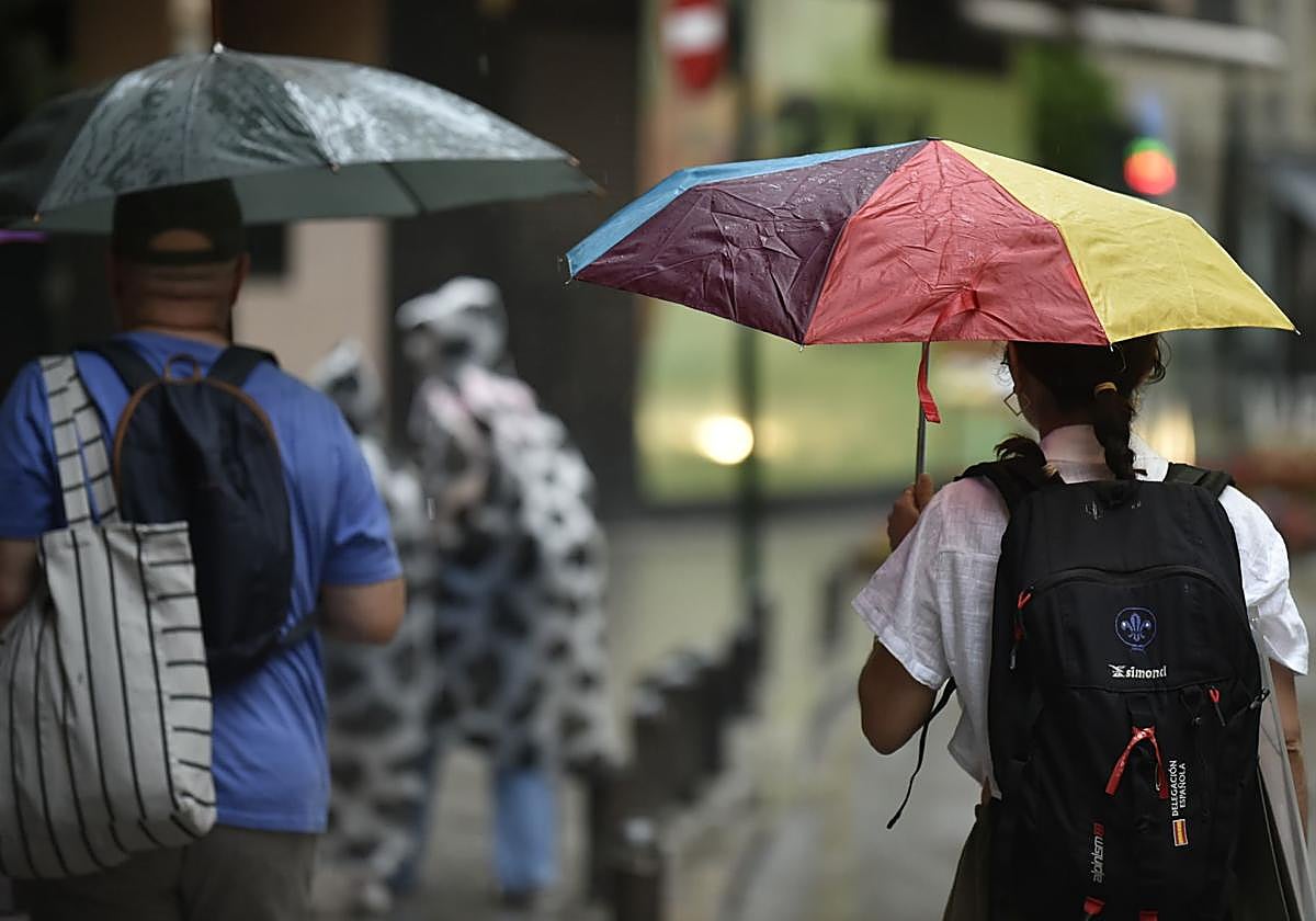 Peatones se protegen de la lluvia mientras caminan por Murcia.