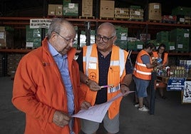 El tesorero y el presidente del Banco de Alimentos comprueban las solicitudes, mientras los voluntarios preparan los kits.