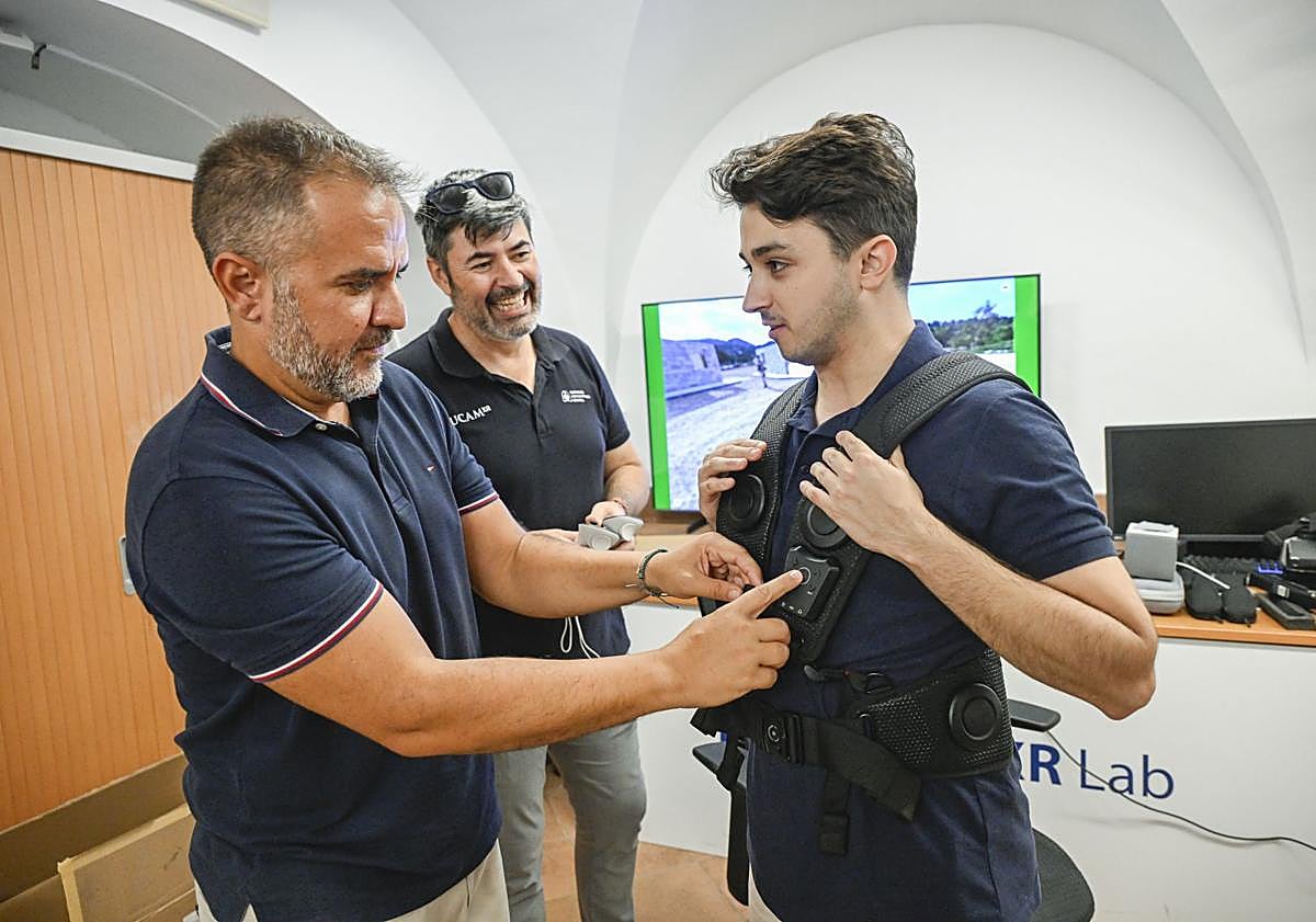 Imagen principal - Arriba: Manuel Pardo coloca un chaleco háptico a Alberto Lanchares. Abajo: El profesor examina algunas de las gafas de realidad virtual de la UCAM.