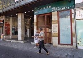 Dos personas caminan frente a la entrada del antiguo local comercial okupado.