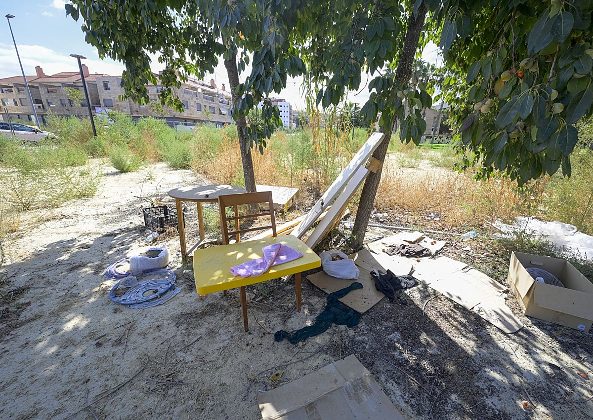 Imagen secundaria 1 - En la imagen superior, varios transeúntes pasan por delante de un tramo forzado de la valla perimetral. Abajo, detalle una zona central de la zona verde, con muestras de haber sido usada para pernoctar al raso. En la fotografía inferior, un vecino señala las casas vecinas cercanas a un entorno cubierto de malezas y con restos de palés de madera rotos.