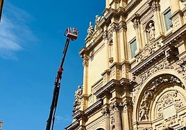 Una camión grúa con cesta se acerca a la fachada de la antigua colegiata para la retirada de las plantas.