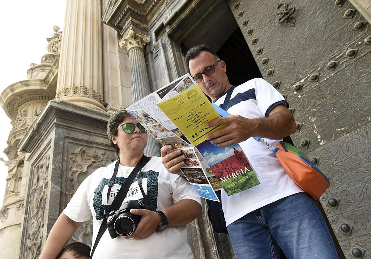 Unos turistas consultan un mapa junto a la Catedral de Murcia.