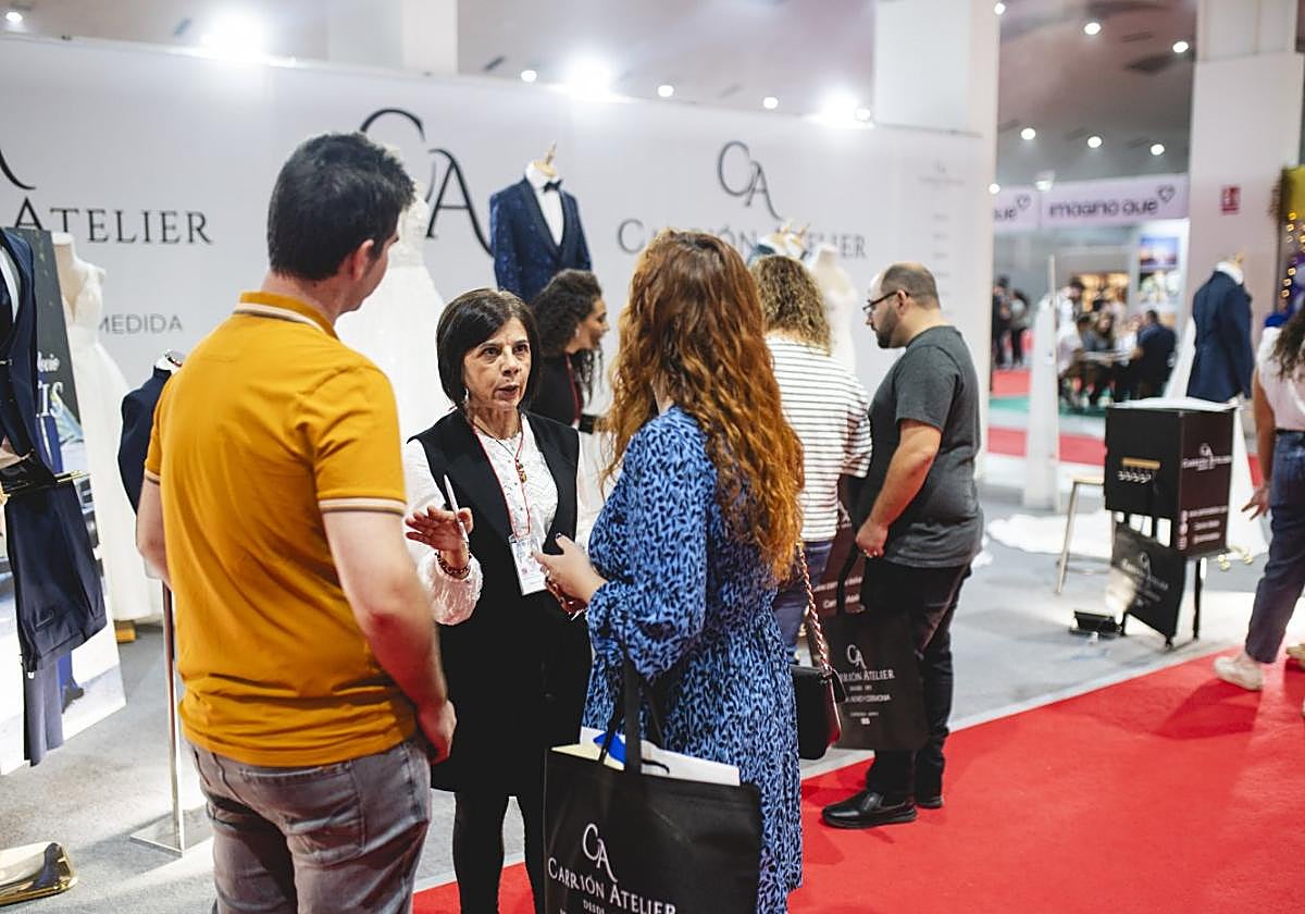 Una pareja charla con una expositora de una marca de moda en Boda&Celebraciones.