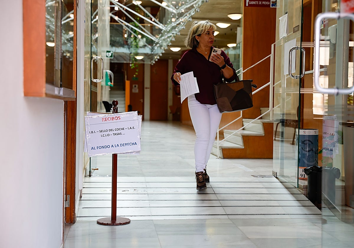 Una ciudadana pasa junto a un cartel informativo sobre el pago de tributos en el Ayuntamiento.