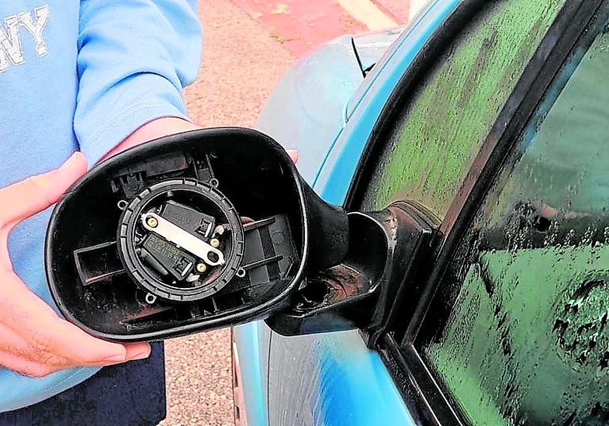 Un vecino muestra el retrovisor destrozado de un vehículo.