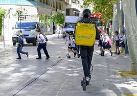 Un grupo de escolares cruza el carril bici del paseo Alfonso X de Murcia, justo al paso de un 'rider' de reparto.