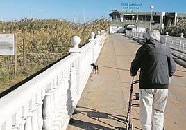 Un hombre pasea a su perro junto al acceso principal al puerto deportivo de Los Nietos.