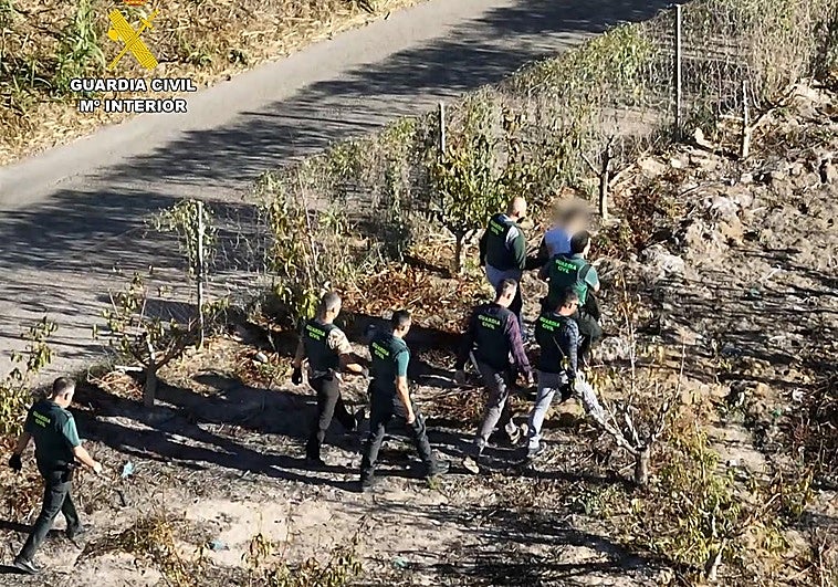 Los guardias civiles conducen al detenido a un coche patrulla tras interceptarlo.