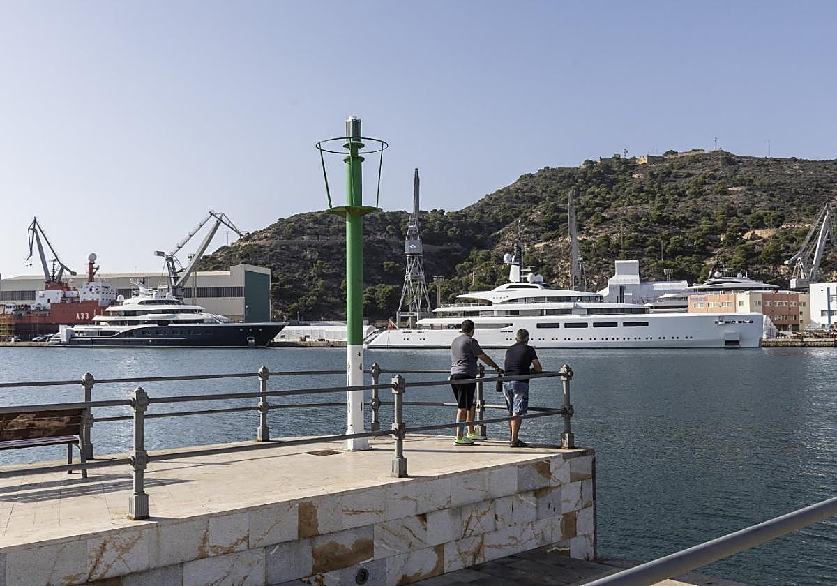 Dos personas observan los yates en reparación del astillero desde el antiguo Club de Regatas.