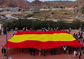 Alumnos y profesores del instituto Bartolomé Pérez Casas despliegan la bandera de España en el patio del centro.