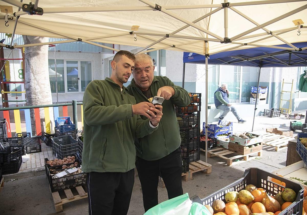 Pedro y Jesús, vecinos de puesto en el mercado, ven noticias de la previa del Cartagena-Murcia en una aplicación, durante una pausa.