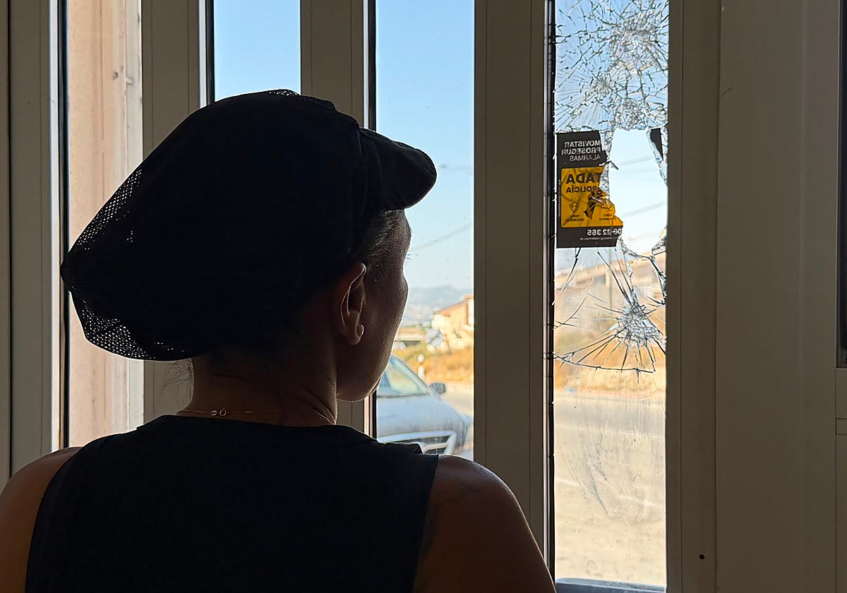 La propietaria del bar Fenazar mira el cristal roto de la puerta de su establecimiento.