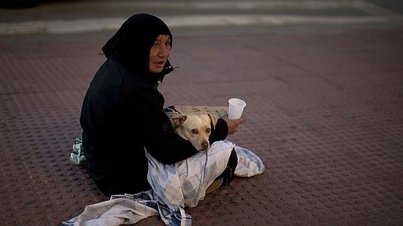 Una mujer, junto a su perro, pide limosna en una calle de Málaga.