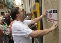 El cura Joaquín Sánchez pega un cartel en una oficina bancaria en Murcia. / Foto: Nacho García / Vídeo: Raúl Hernández