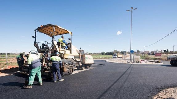 Cuatro operarios asfaltan la rotonda construida en el cruce del Camino del Sifón con la carretera de Molino Derribao.