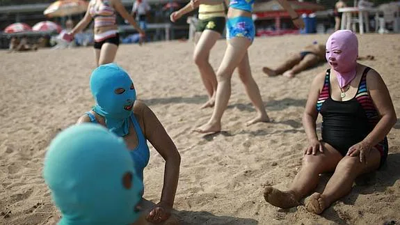 Mujeres chinas se protegen la cara del sol con unas máscaras de nylon ('Face-kini') durante su estancia en una playa de Qingdao, en China. 