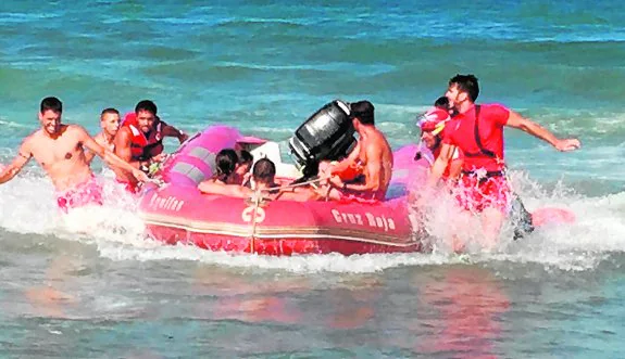 Voluntarios de Cruz Roja trasladan a la orilla a un grupo de bañistas rescatados en unas rocas en La Carolina de Águilas. 