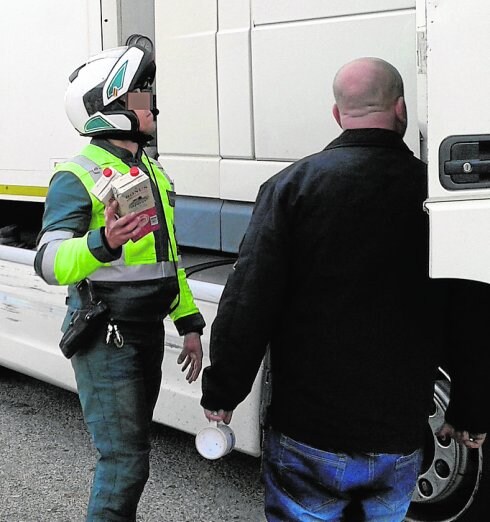 Un agente de la Guardia Civil, con dos de los cartones de vino hallados en el interior del camión; a la derecha, el conductor.