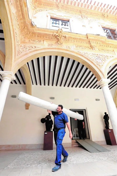 Un operario, cargado con uno de los cortineros de madera, cruza el patio porticado del palacio.