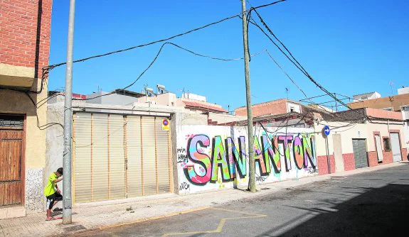 Un chaval pasa junto a una tapia en la que está rotulado el nombre del barrio, en el centro de San Antón. 