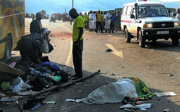 Los pasajeros de un autobús siniestrado recogen sus enseres junto al cadáver de una víctima.