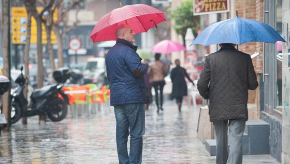 Un hombre se protege de la lluvia en una céntrica calle de Murcia.