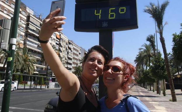 Dos jóvenes se hacen una foto con el panel del termómetro de una calle de Córdoba. 