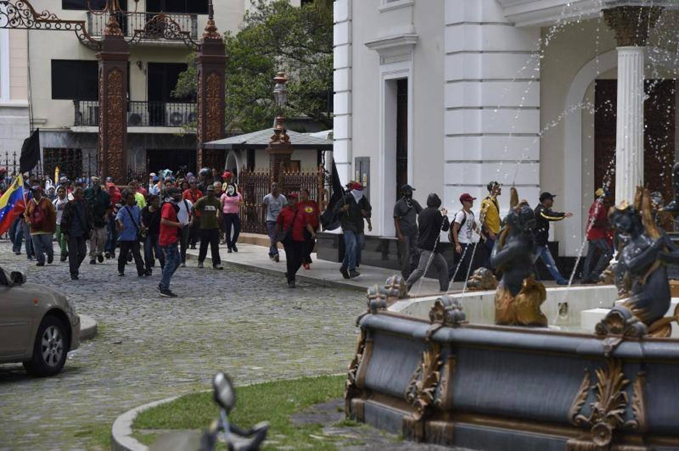 Decenas de personas, algunas encapuchadas, con palos y tubos, y vestidas de rojo, entraron a los jardines de la Asamblea Nacional y detonaron cohetes de fuegos artificiales, desatando el caos