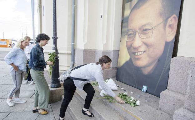 Varias personas dejan flores y velas frente a una imagen del disidente chino en extranjero. 