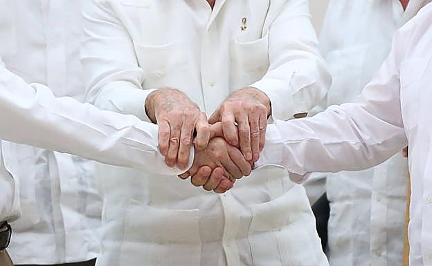 Raúl Castro sostiene las manos del presidente de Colombia, Juan Manuel Santos, y del líder de las FARC Rodrigo Londono. 