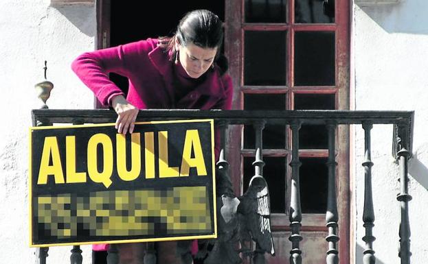 Una mujer cuelga en el balcón un cartel para alquilar su vivienda.