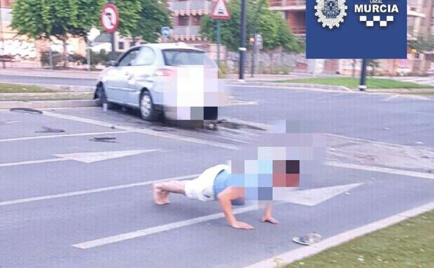 El conductor haciendo flexiones con el coche siniestrado de fondo.