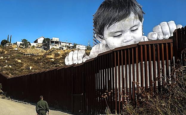 Un gente estadounidense observa el mural de un niño levantado en la frontera con México.