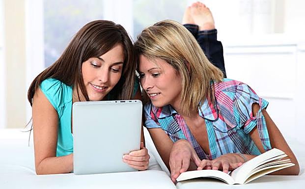 Dos jóvenes con un libro electrónico y otro en papel.